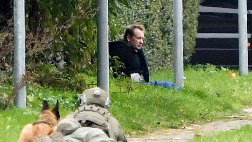 A police officer watches Peter Madsen as he sits on the side of a road after being apprehended following his escape.
