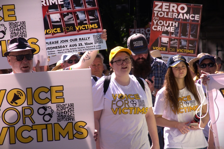 A crowd of people wear shirts that read 'voice for victims' while marching through Brisbane