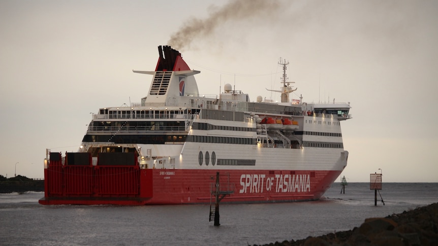 A big red and white ferry sails away from the camera at dusk.