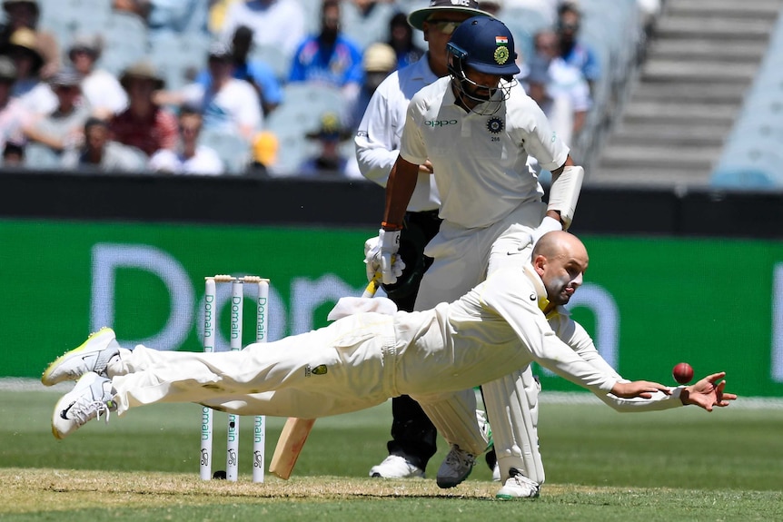 Indian batsman Cheteshwar Pujara watches Australian bowler Nathan Lyon dive in the field.