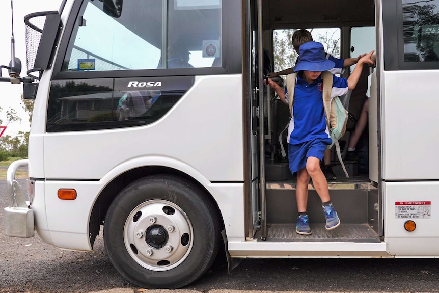 Young student in school uniform steps off a bus onto the road