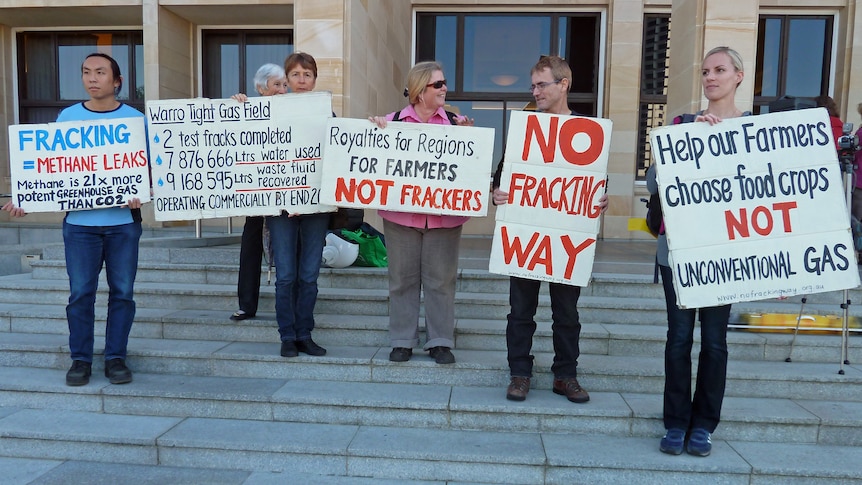 People holding signs protesting about unconventional gas, standing outside a building.