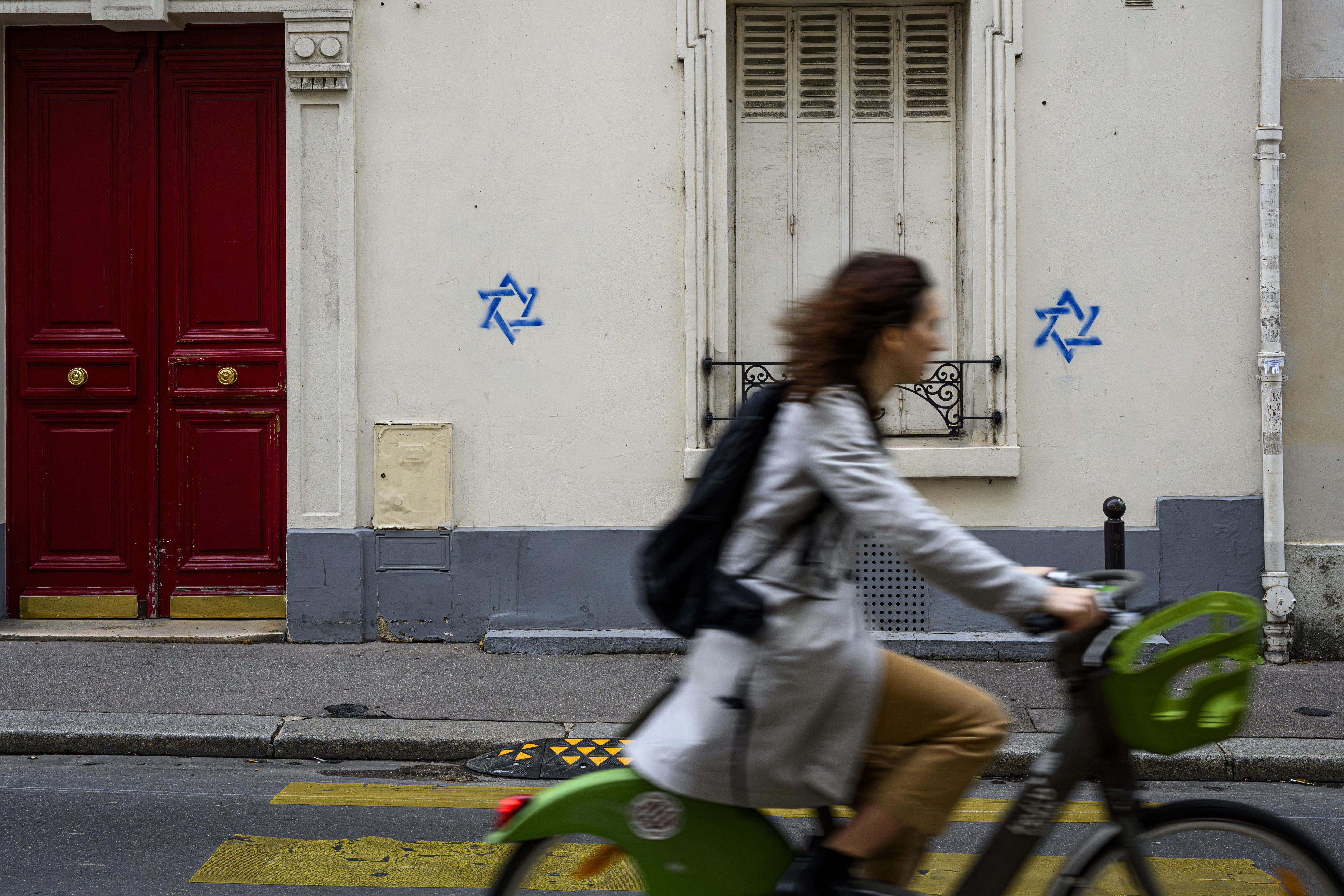 Two blue stencilled stars are painted onto a white building as a cyclist moves past them on the street.