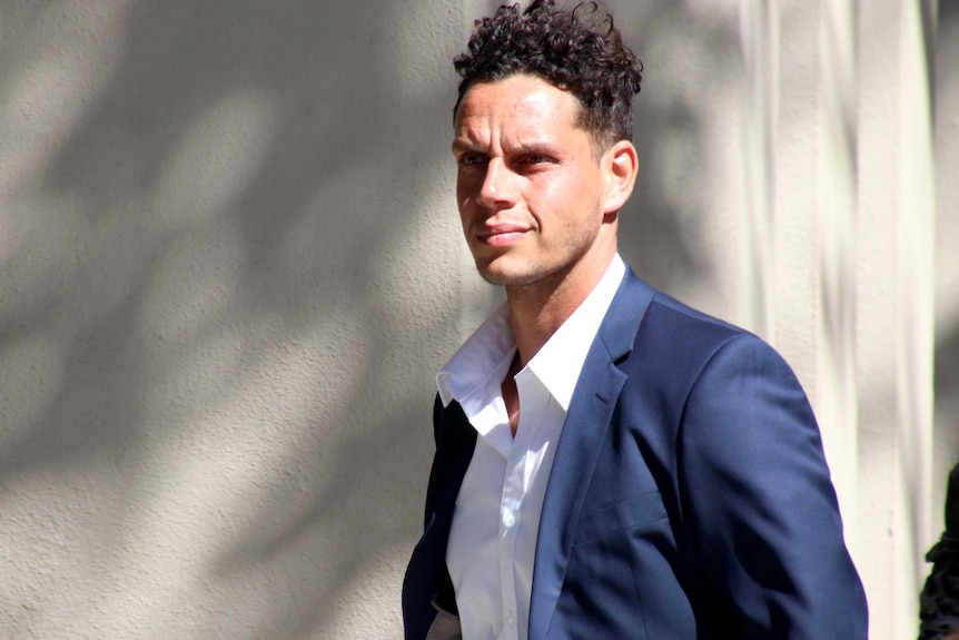 Michael Johnson walks outdoors wearing a blue suit and white shirt.