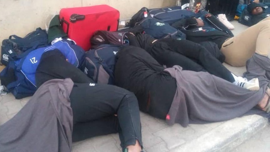 Players sleep on the street surrounded by their luggage.