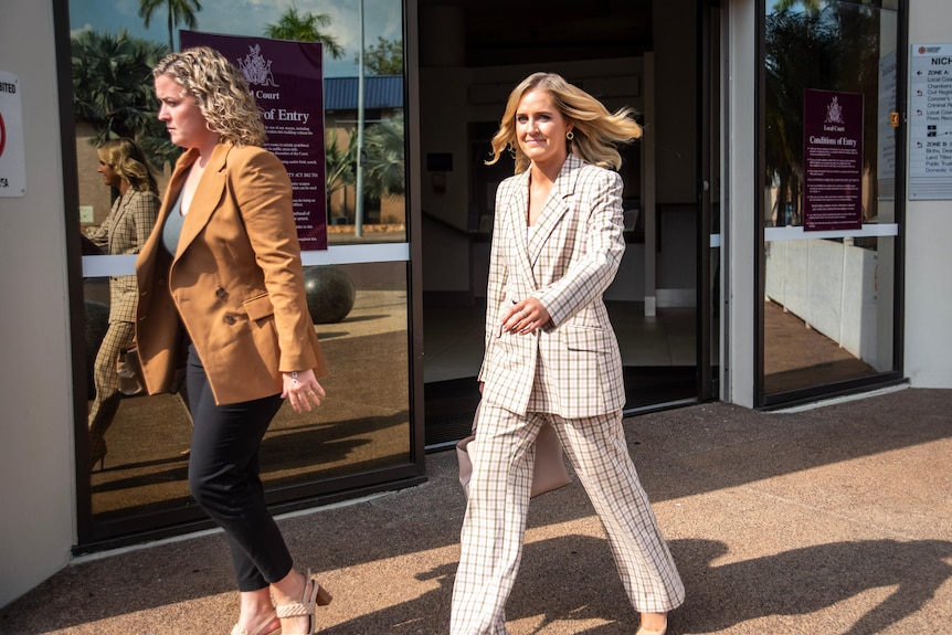 Woman in chequered suits walks out of the front door of a court next to a reporter 