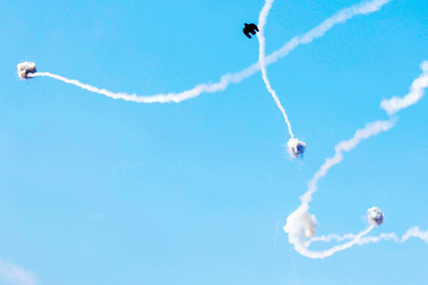 Missiles with trails of smoke being hit in daylight sky.