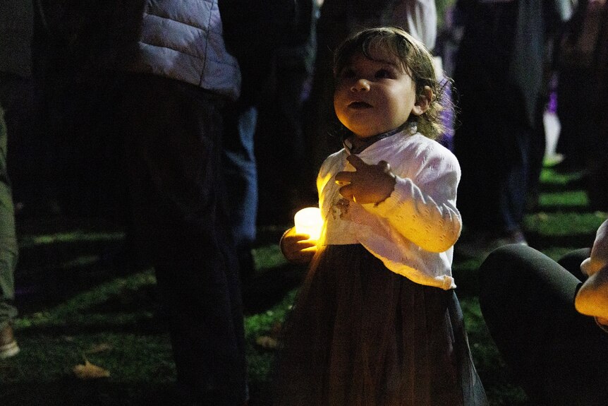 Little girl holds a candle at a vigil for domestic violence victims.