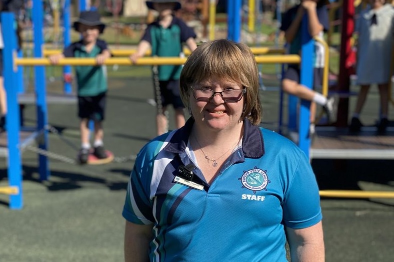 A woman in a blue shirt stands in front of a school playground
