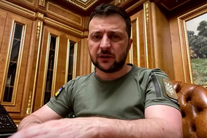 Ukrainian President Volodymyr Zelenskyy sits at his desk in a green military t-shirt, talking to the camera