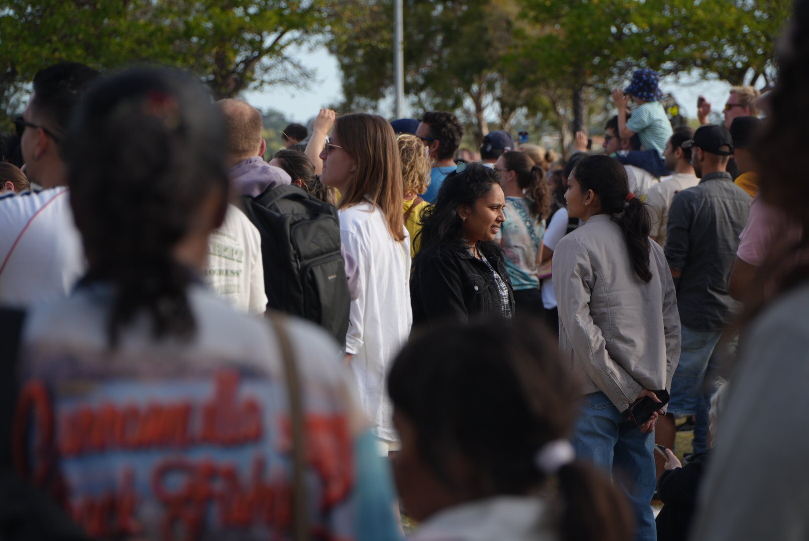Una multitud de personas en un parque público cuando se acerca el anochecer.