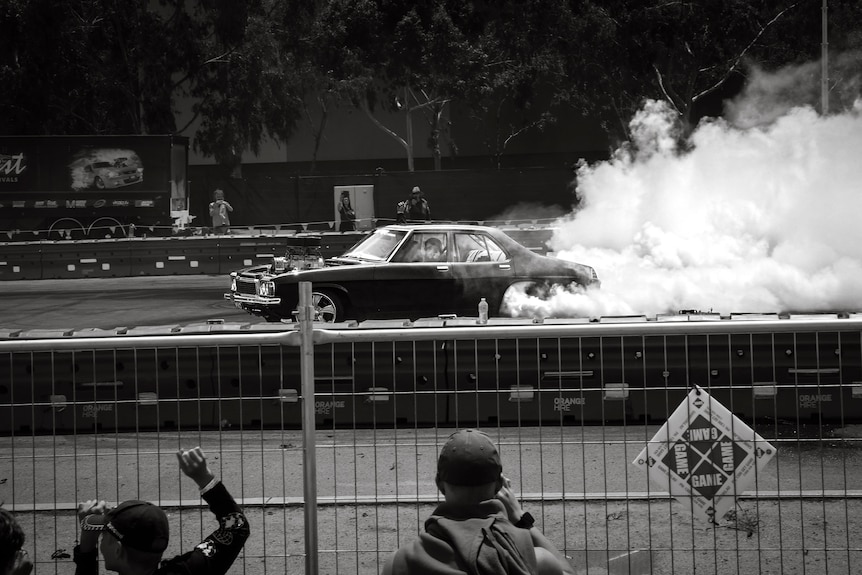 A black and white photo of a car doing a burnout in front of a crowd.