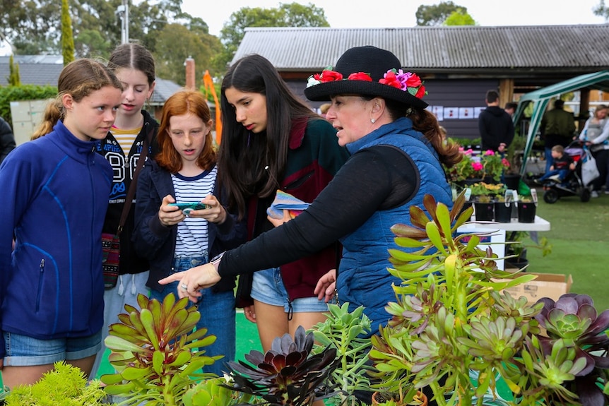Three girls and one woman look at a plant stall at a school fete.