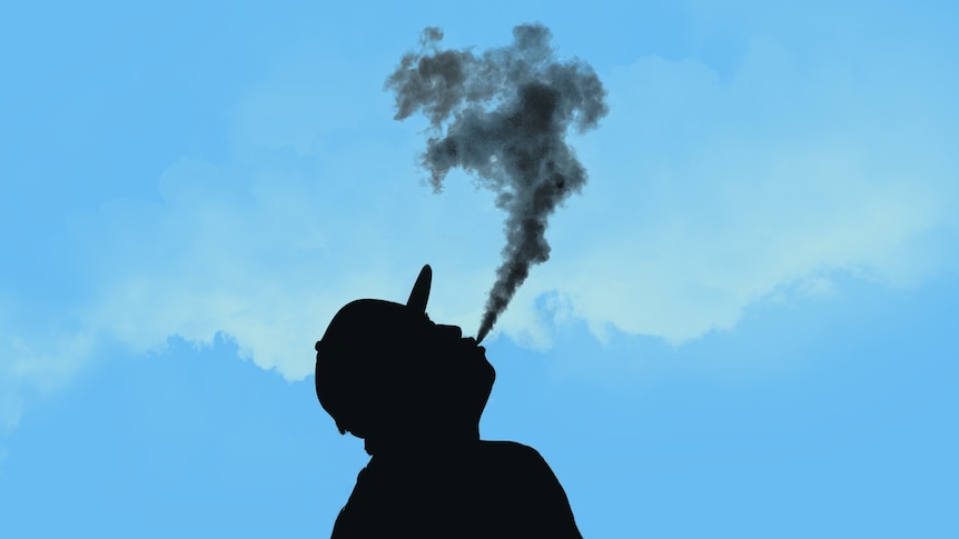 A silhouette of a man vaping against a blue sky, he is wearing a cap.