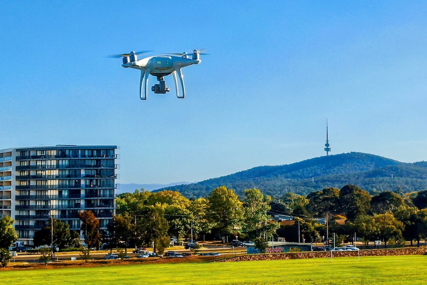 A drone flying above a playing field in Canberra. An apartment building and Black Mountain Tower is in the background.