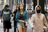 People walk down a city street wearing face masks.