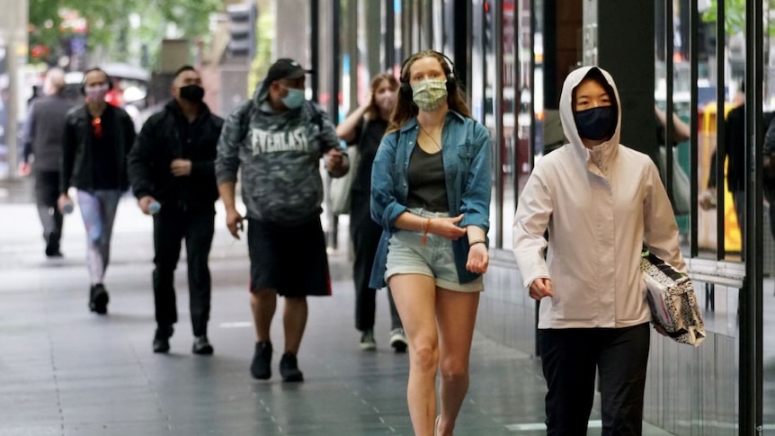 People walk down a city street wearing face masks.