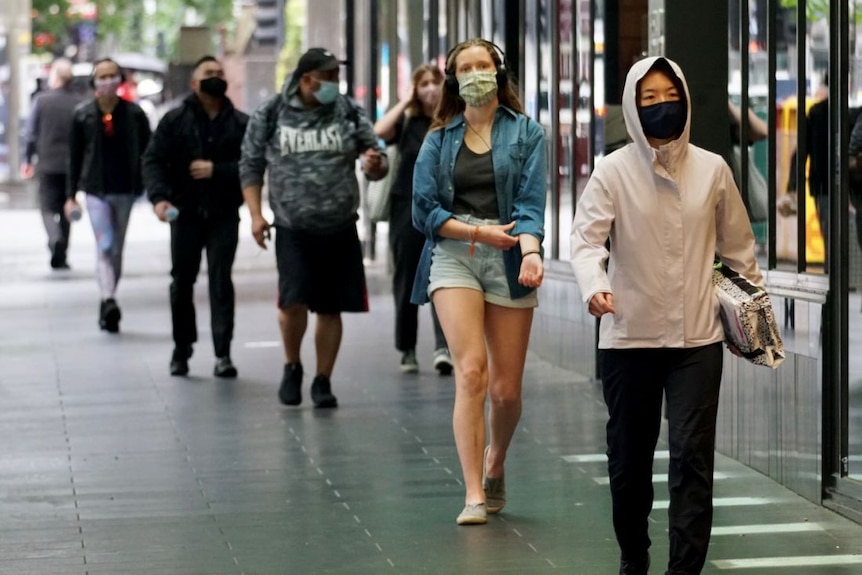 People walk down a city street wearing face masks.