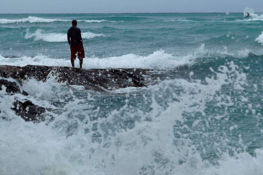 Man stands on rocks as rough surf brews in Hawaii as Hurricane Lane nears