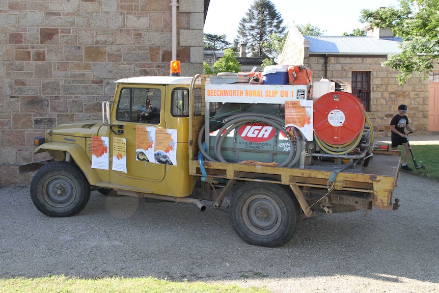 Old mustard-coloured ute with homemade water tank and hose attached to tray
