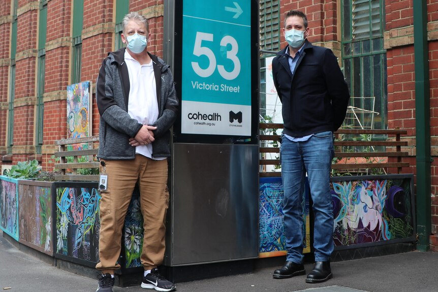Two men in surgical masks standing in front of a building