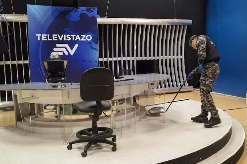 A man wearing an army uniform and protective armour uses a hand-held device to look under a table