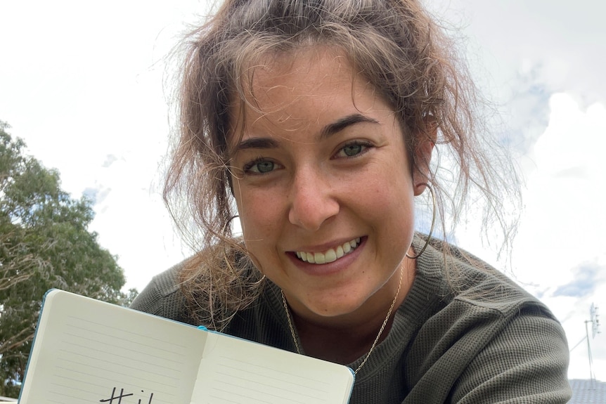A young woman holds a notebook and smiles.