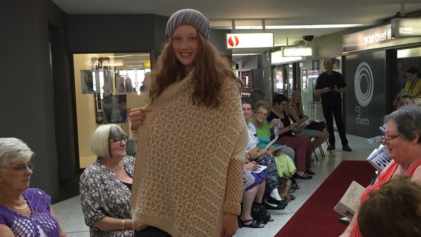 Two women hold a woollen knitted cardigan and shawl up for viewing, at a fashion show in Penrith New South Wales