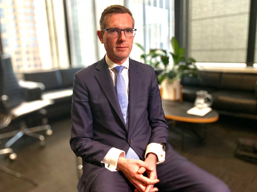 NSW Treasurer Dominic Perrottet sits in a large office wearing a suit.