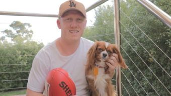 Former Essendon and Brisbane footballer Josh Green sits on stairs with a football and a dog.