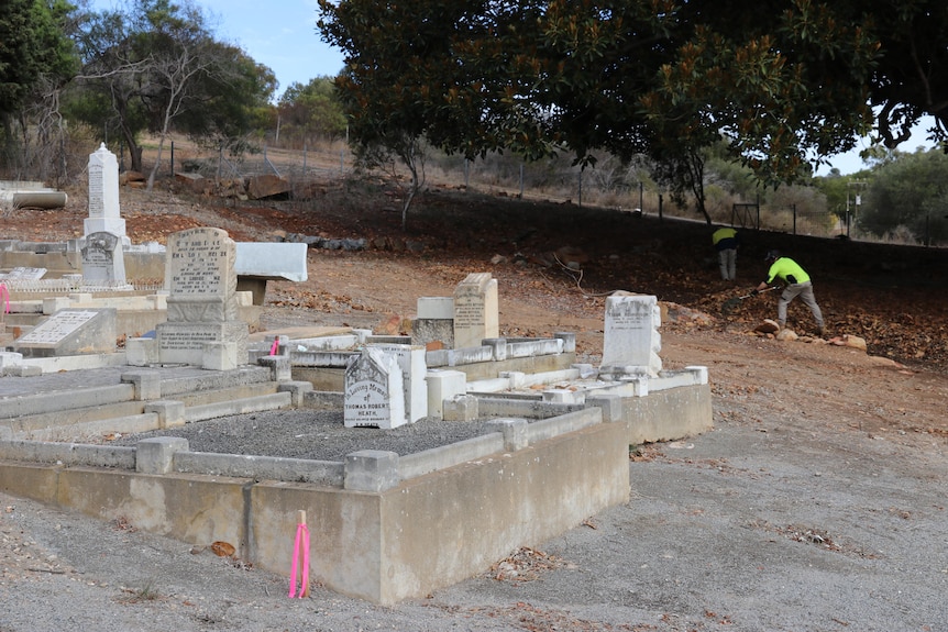 two men in hi-vis vests work at a cemetery 