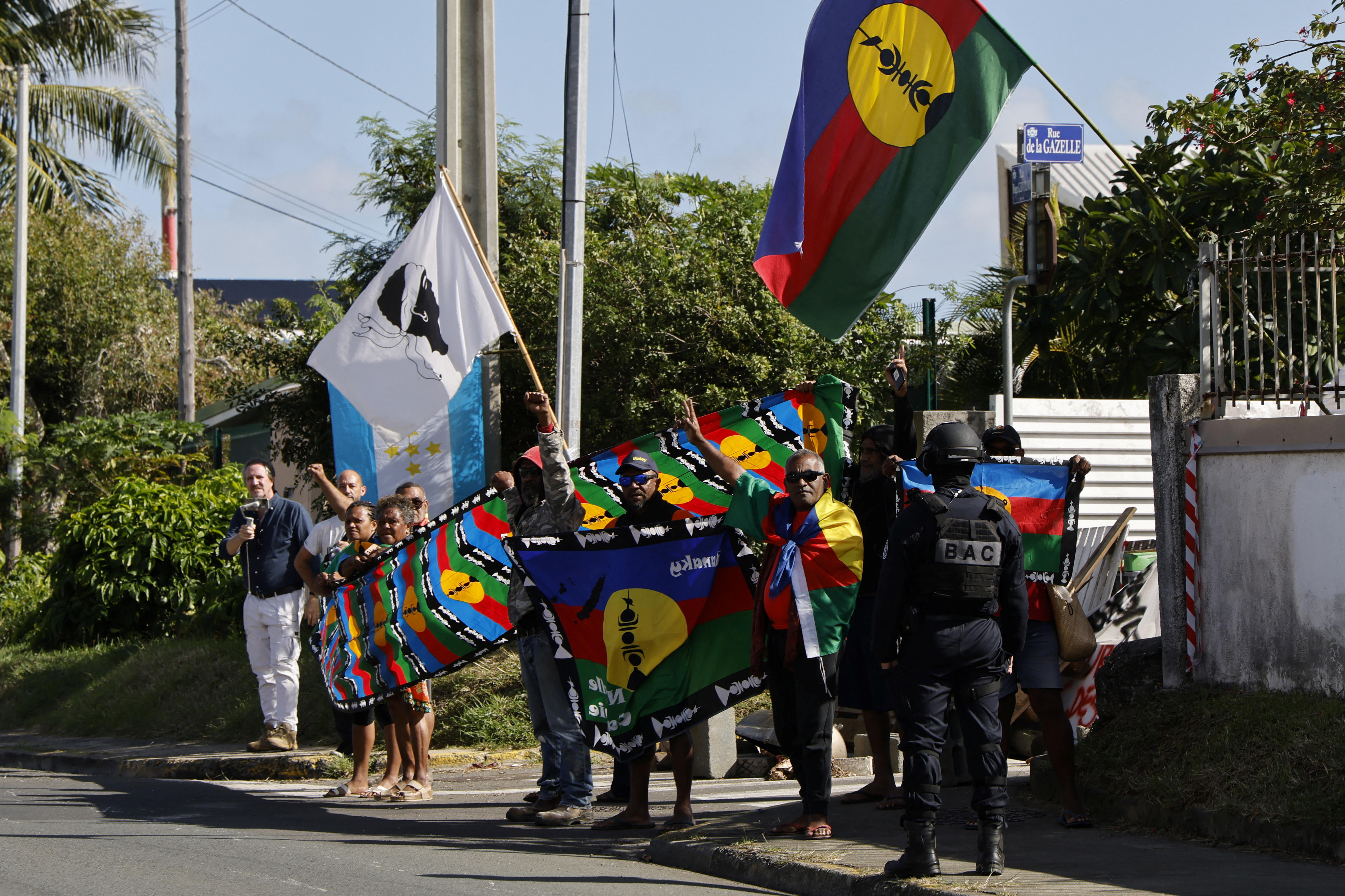 A group of protesters on a sidewalk waving flags. A policeman stands near them.