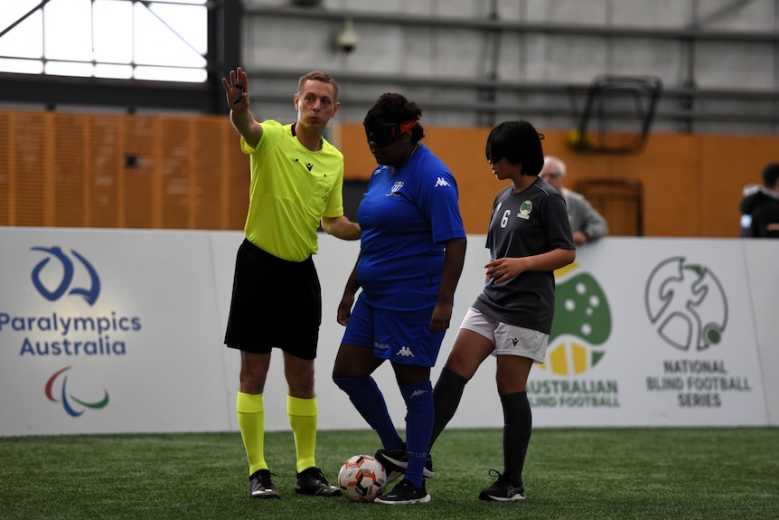 A female blind footballer prepares to kick the ball, while another player stands close by.