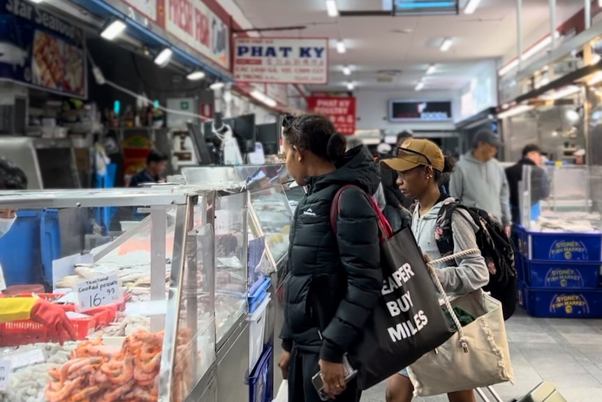 An inside view of Footscray market showing a meat deli selling pork and red meat, a woman and her son at the counter.