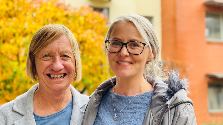 Two women stand together and smile 