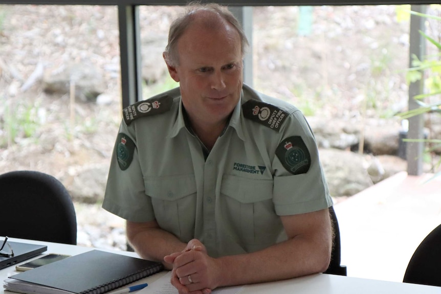 A man sits at a table wearing a green Forest Fire Management uniform.