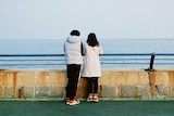 couple wearing warm clothes stand together looking out at the water
