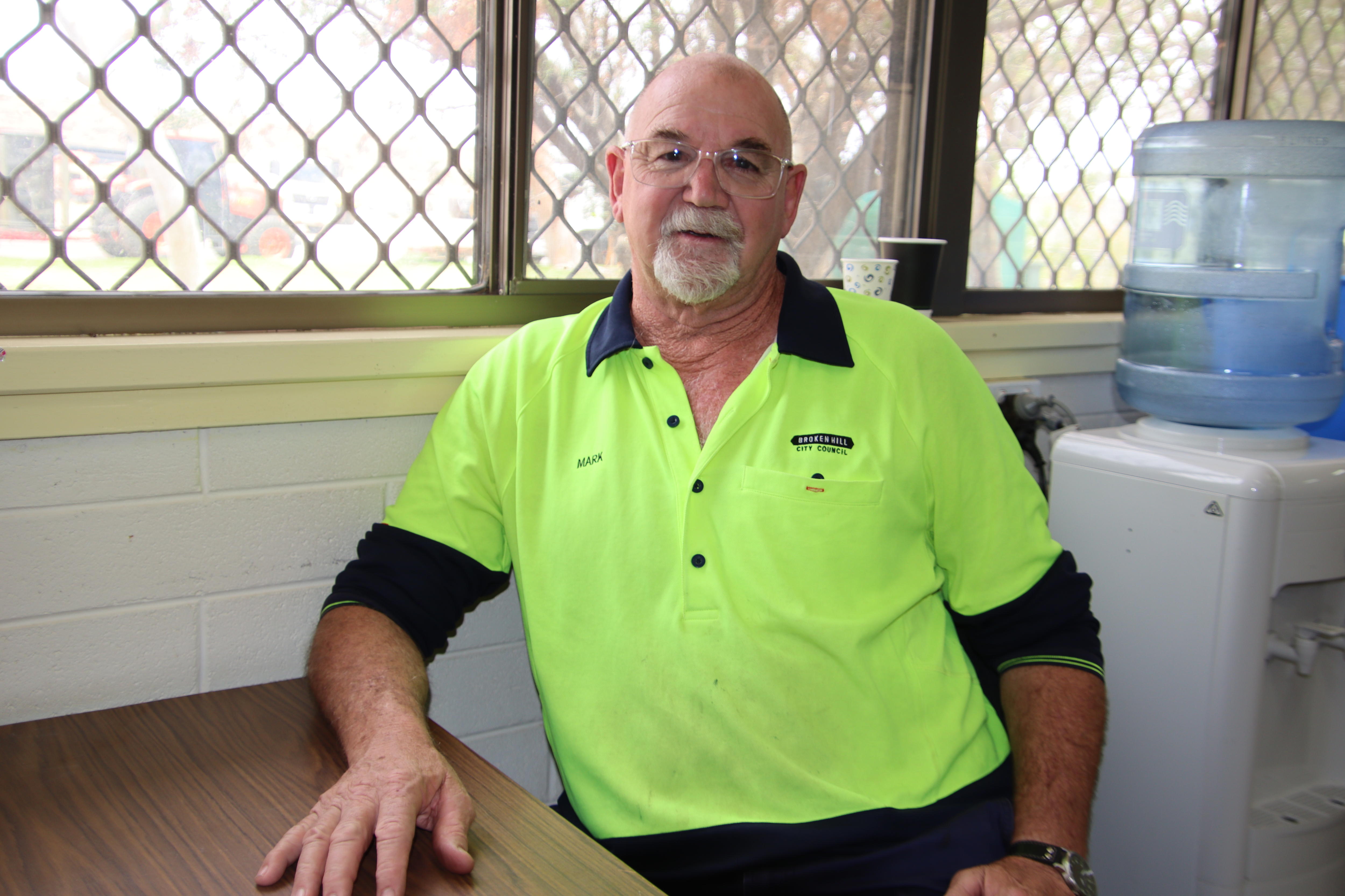 Un hombre mayor calvo con barba y un top de neón se sienta en una mesa