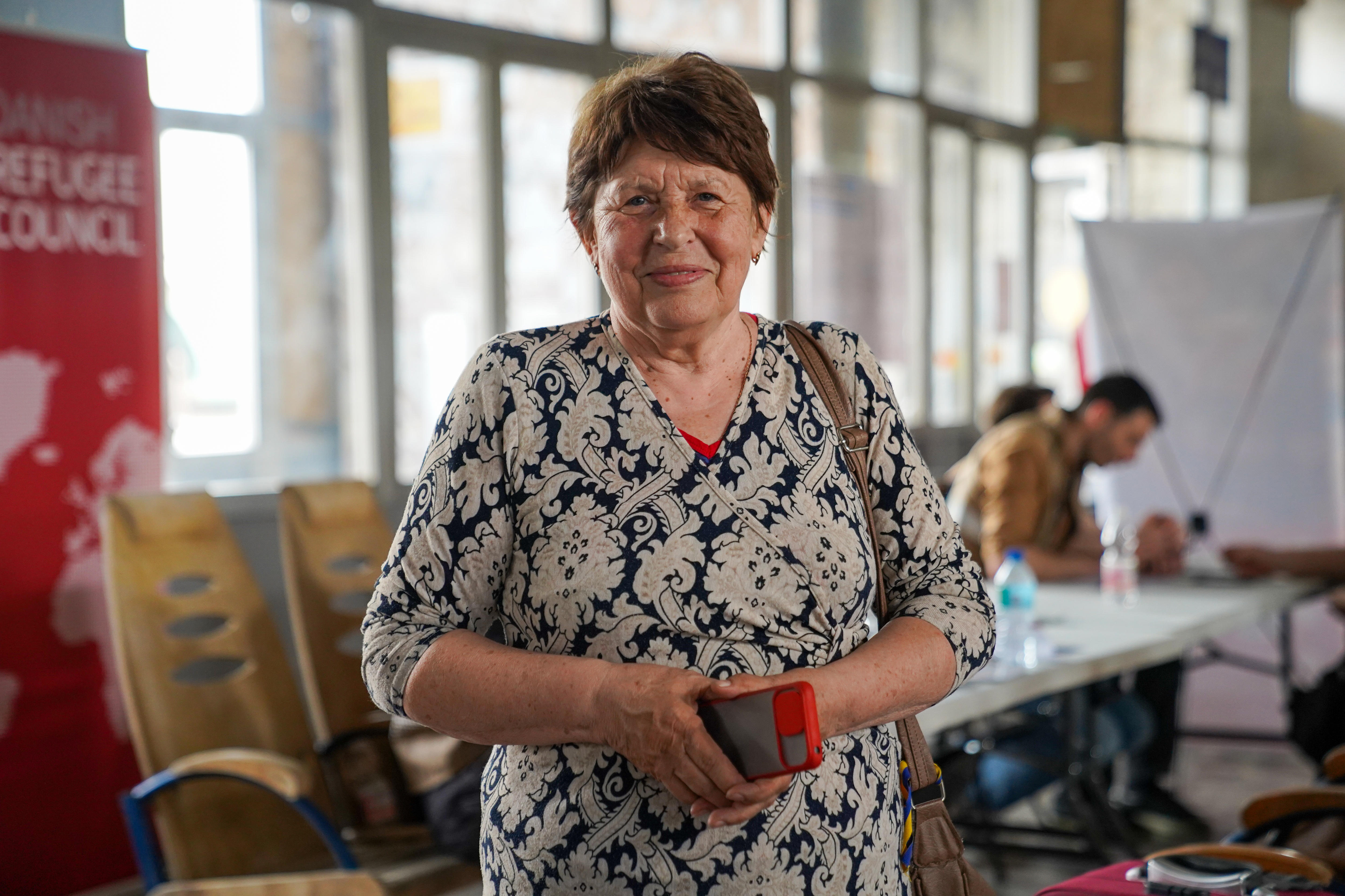 A close up of a smiling woman holding her phone and wearing a floral shirt.