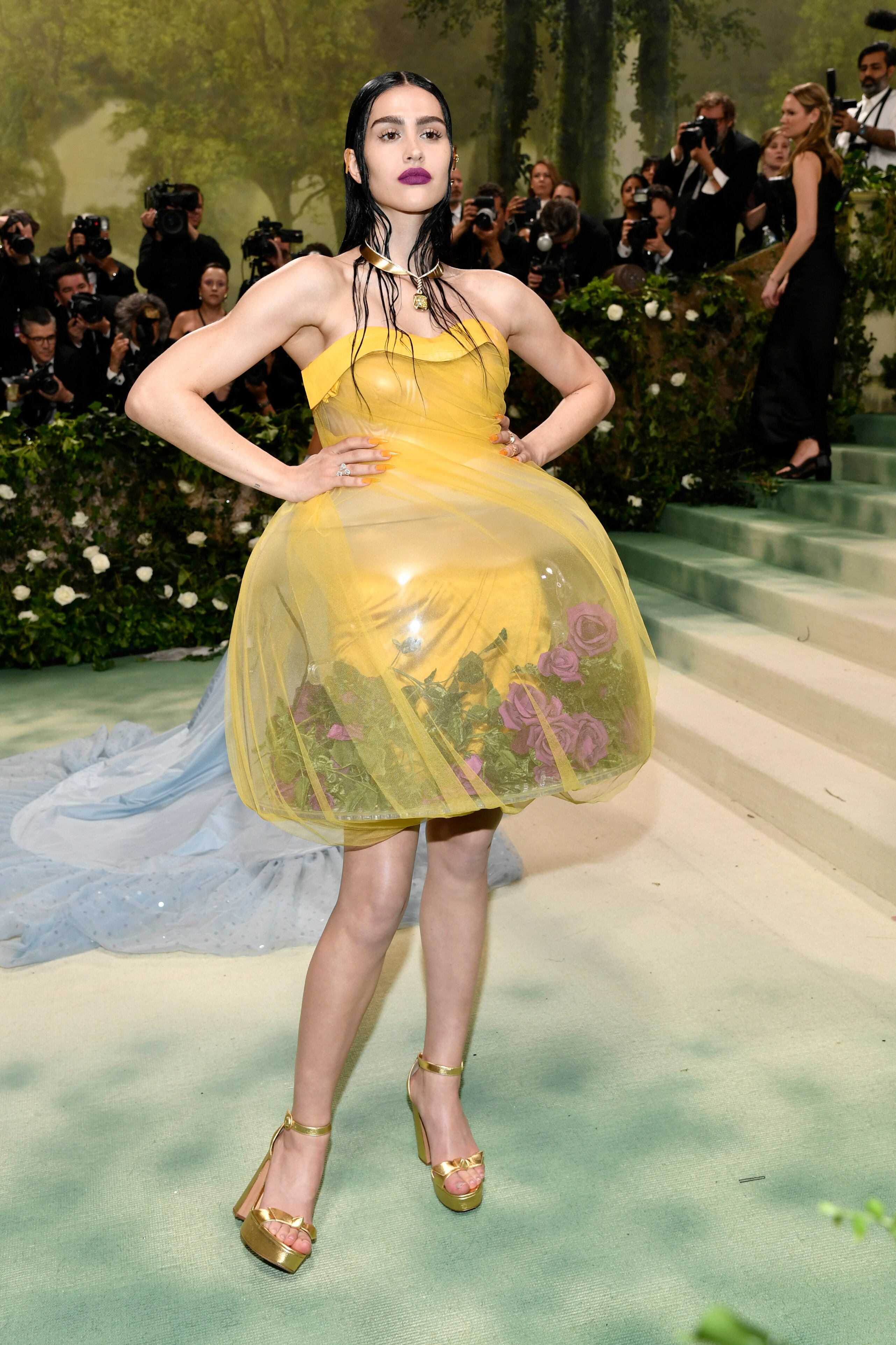 Amelia Gray wearing a yellow strapless mini dress, with the skirt being a glass bowl with pink roses in it