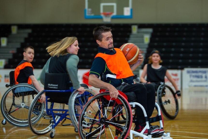 Wheelchair basketballer clutching ball, spins away from an opponent caught tolling the other way.