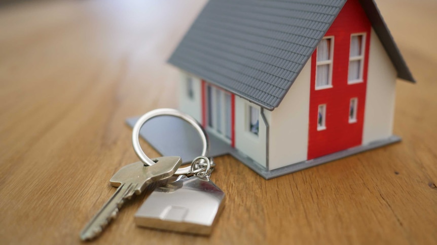 A gold key in front of a small white and red model house with a grey roof.