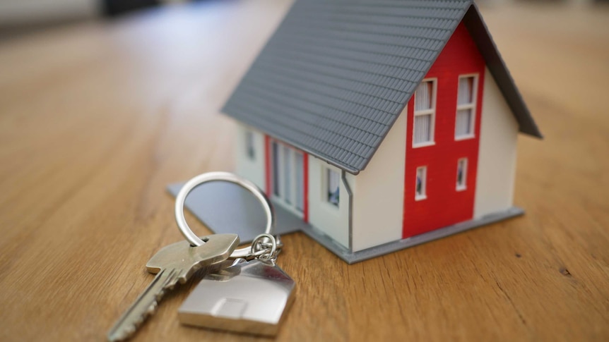 A gold key in front of a small white and red model house with a grey roof.