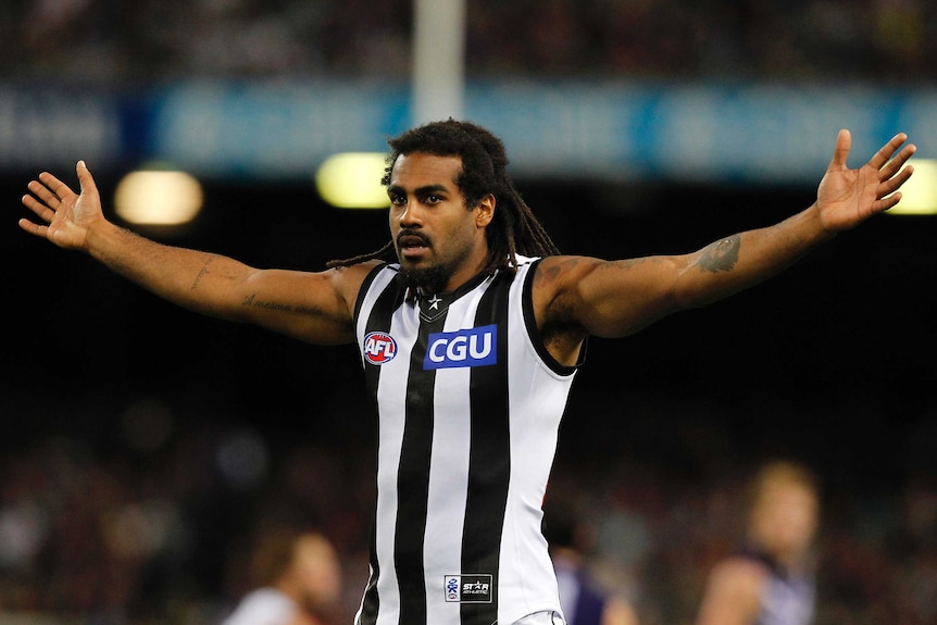 An AFL player holds his arms out to the sides while on the field.