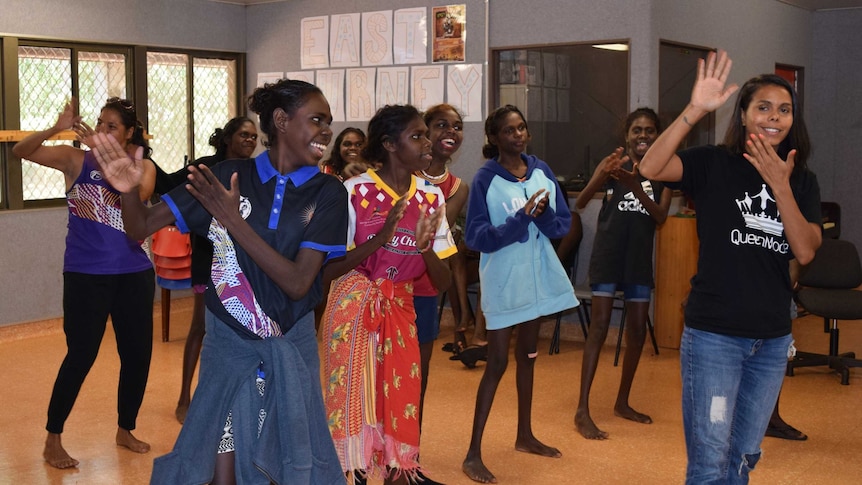 A group of Indigenous students are dancing, with instructions from their mentor, Elena. They are smiling and clapping.