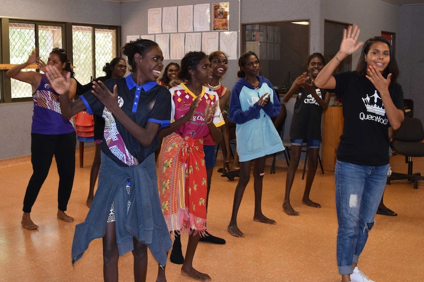 A group of Indigenous students are dancing, with instructions from their mentor, Elena. They are smiling and clapping.