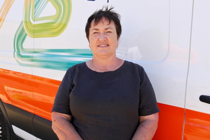 Midshot of a woman in a black dress in front of a Western Power van. 