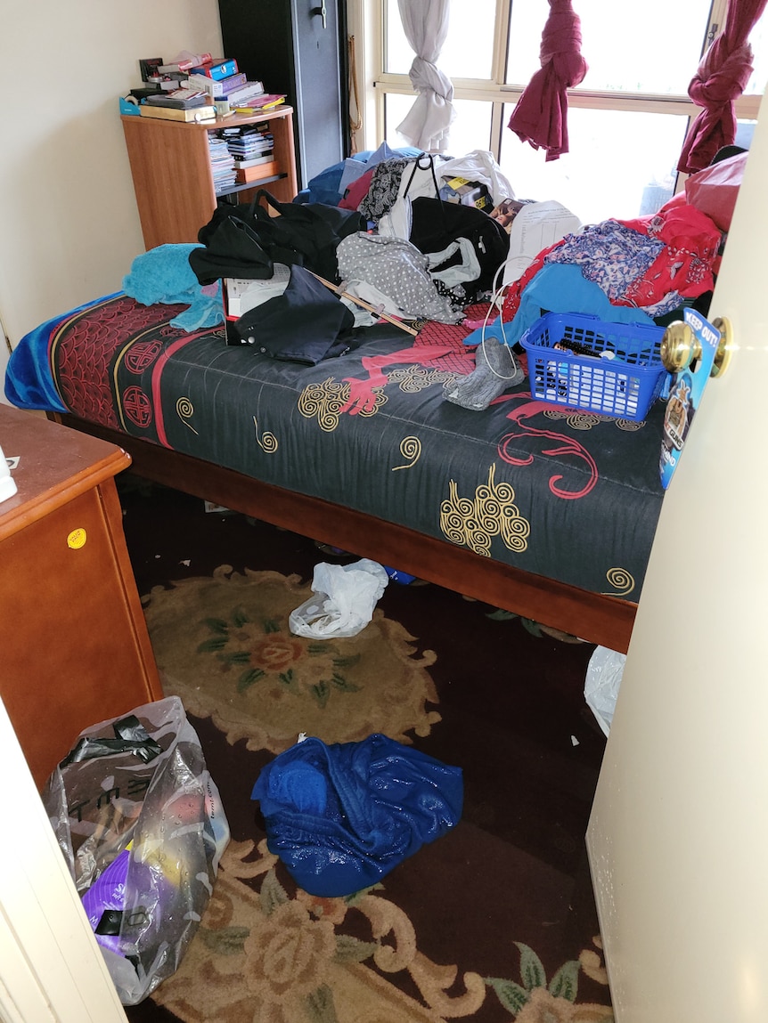 Personal belongings are piled on top of a bed as water creeps underneath.