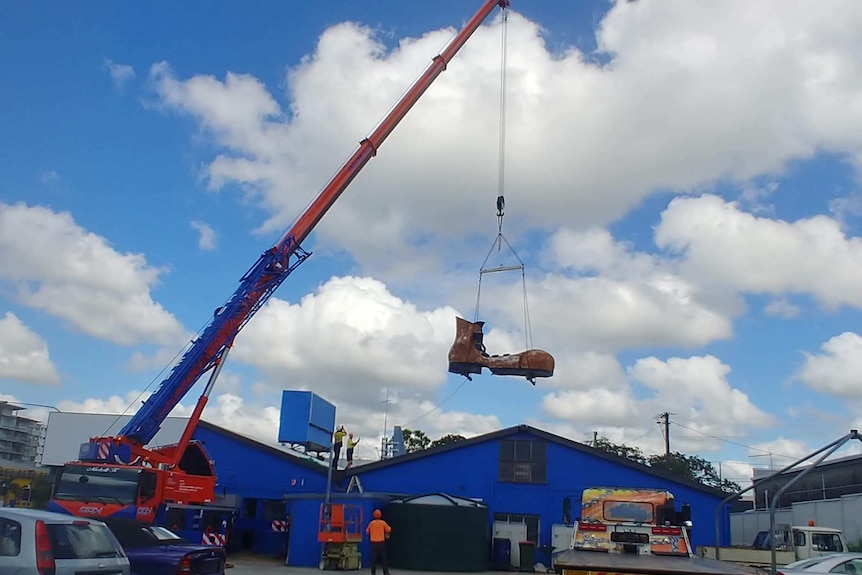 An orange crane lifts the boot from its spot atop the car yard on Gympie road.