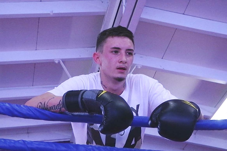 Young man wearing boxing gloves stands at the ropes